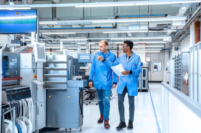 Mitarbeiter der Zollner Elektronik AG gehen durch Fertigungshalle in ESD-Schutzbekleidung, Hinweis auf Zusammenarbeit im Team.