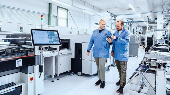Zwei Mitarbeiter gehen durch eine Produktionshalle und tauschen sich aus