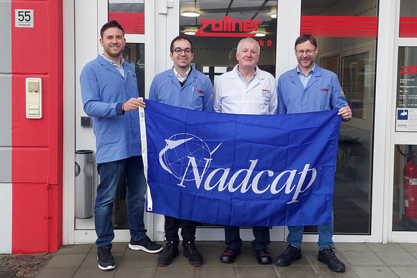 Vier Personen in Arbeitskleidung halten Nadcap-Banner vor dem Eingang der Zollner Elektronik AG.