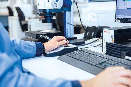 Mitarbeiter führt Restschmutzanalyse nach VDA 19 an einem Arbeitsplatz mit Mikroskop und Computer durch.