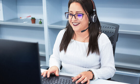 Frau sitzt im Büro mit Headset und telefoniert