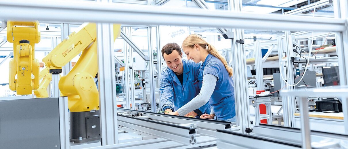 Techniker arbeiten an Fertigungsanlage mit Industrieroboter für Systemlösungen und Support entlang des gesamten Lebenszyklus.