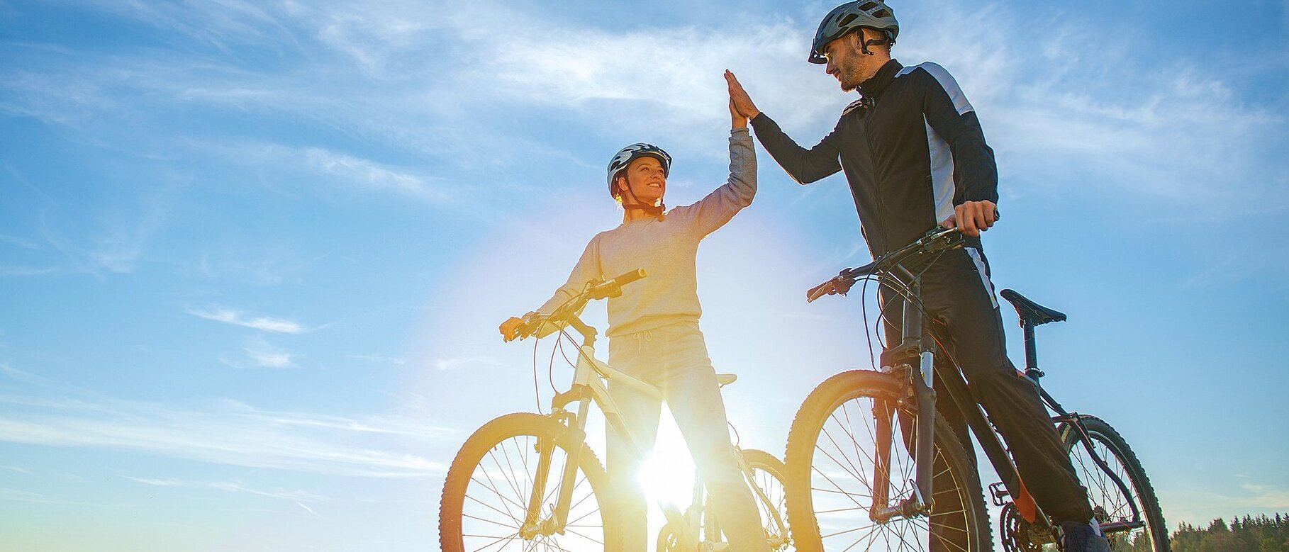 Zwei Mitarbeiter der Zollner Elektronik AG fahren Fahrräder und feiern das Fahrradleasing-Angebot mit High-Five.