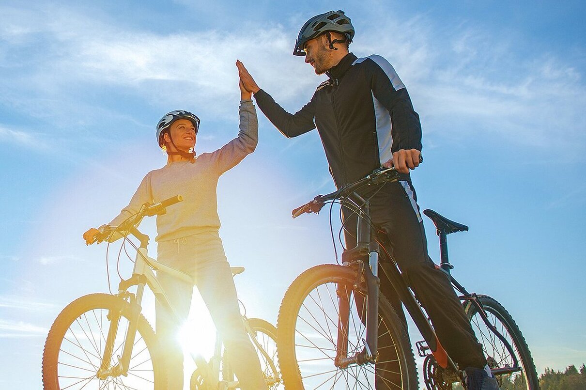 Zwei Mitarbeiter der Zollner Elektronik AG fahren Fahrräder und feiern das Fahrradleasing-Angebot mit High-Five.