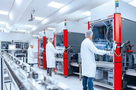 Mitarbeiter in ESD-Schutzkleidung arbeitet in einem Reinraum an einer automatisierten Fertigungslinie für Modul- und Systemmontage in der Elektronikproduktion.