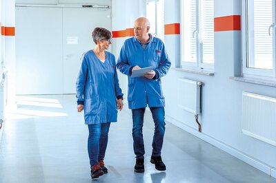 Zwei Mitarbeiter mit Produktionsmänteln gehen durch einen Gang und führen ein Gespräch