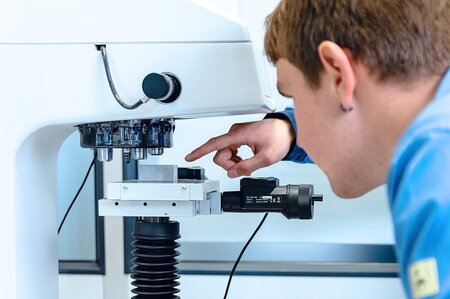 Mitarbeiter führt Härteprüfung an einer Prüfmaschine durch, Test von Metall- oder Kunststoffproben gemäß Standards.