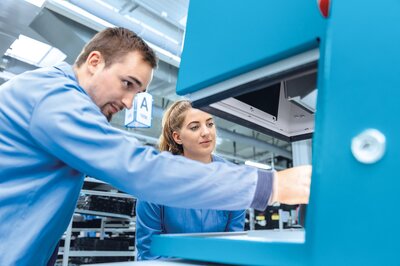 Mitarbeiter der Zollner Elektronik AG arbeiten an Maschine, Symbol für interne Karrieremöglichkeiten.