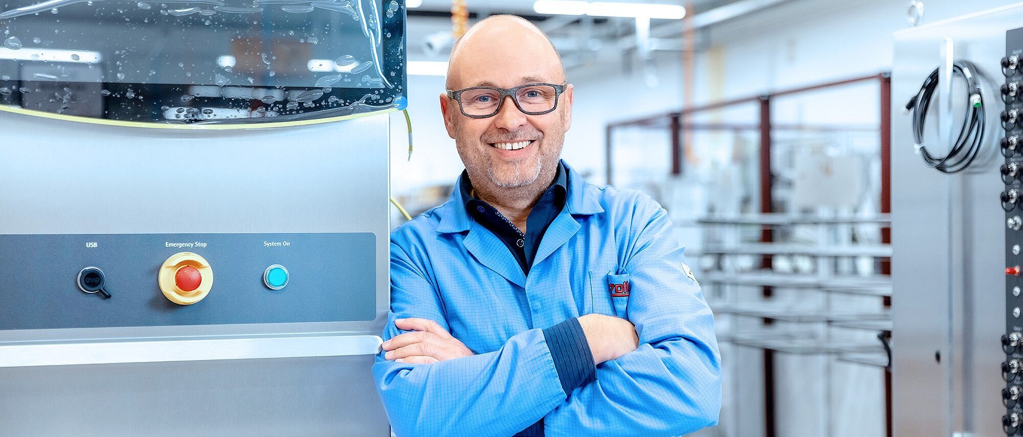 Mitarbeiter der Produktion lehnt sich an eine Maschine und lächelt in die Kamera