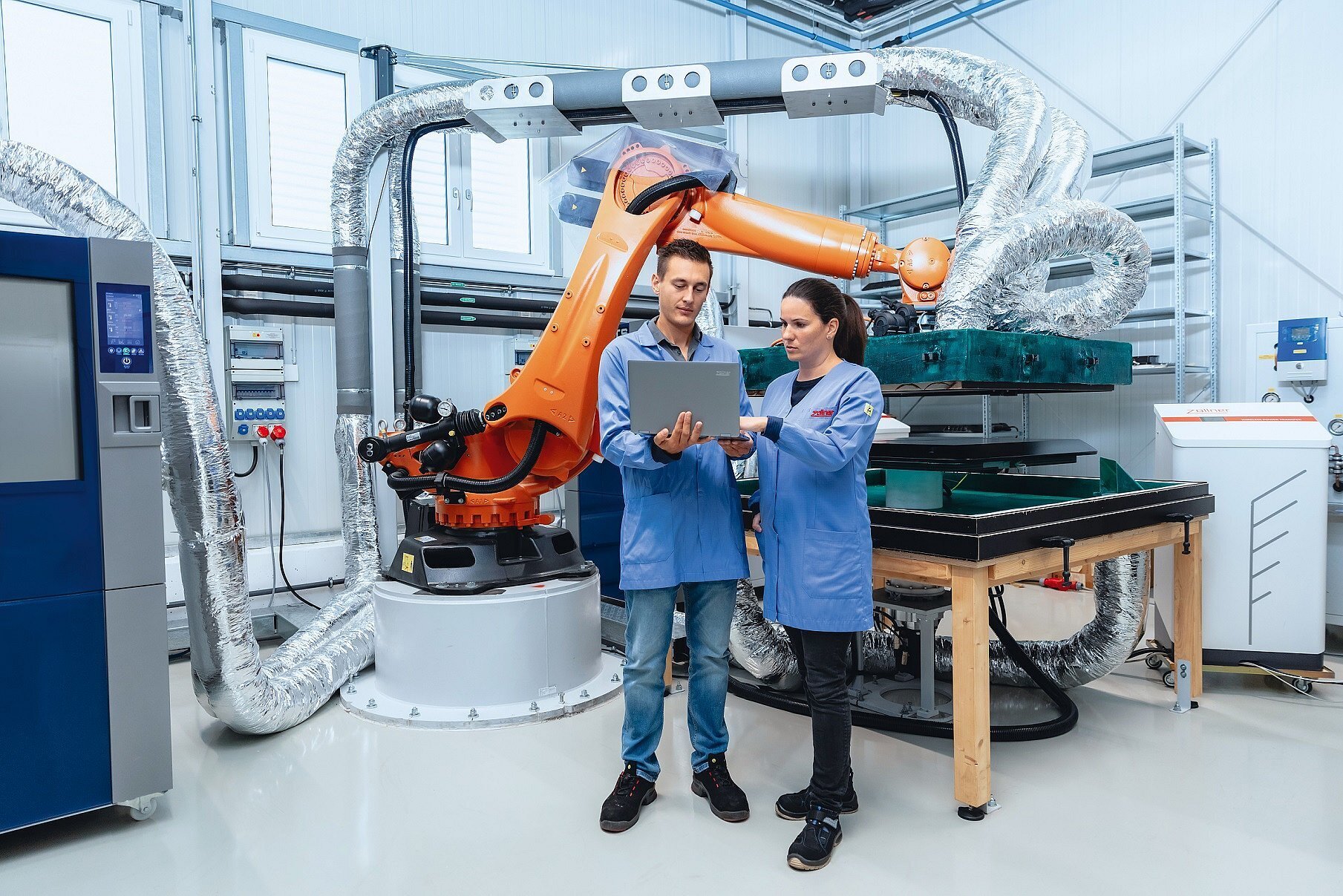 Zwei Mitarbeiter der Zollner Elektronik AG arbeiten mit Industrieroboter und Laptop