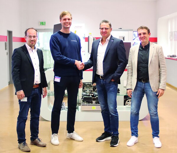Gruppenfoto mit vier Personen, zwei davon geben sich die Hand und lächeln 