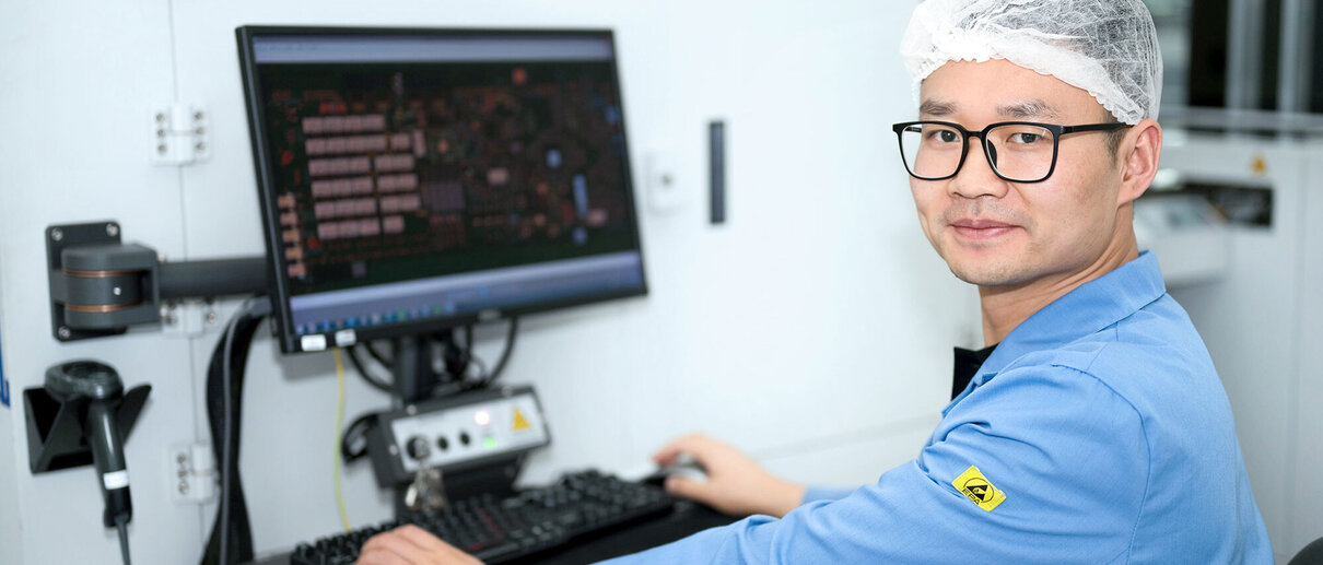 Mitarbeiter in ESD-Schutzkleidung arbeitet an Computer mit Leiterplattenlayout