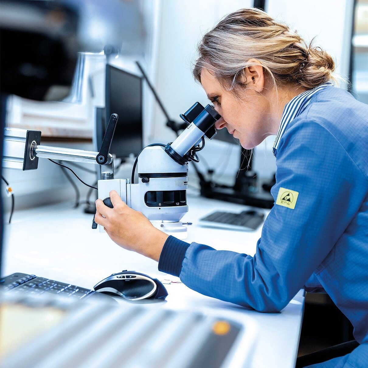 Mitarbeiterin der Zollner Elektronik AG untersucht Materialien unter dem Mikroskop zur Sicherstellung nachhaltiger und transparenter Materialverwendung.