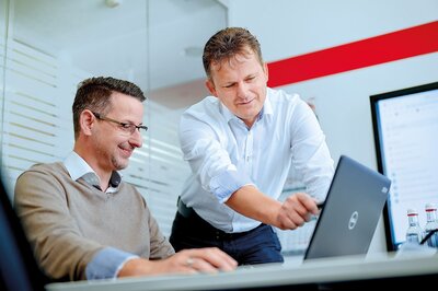 Zwei Mitarbeitende arbeiten am Laptop an Design-to-Cost-Analysen zur Kostenoptimierung in der Produktentwicklung.