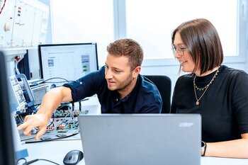 Zwei Mitarbeiter arbeiten an Elektronikentwicklung und Simulationen am Computer.
