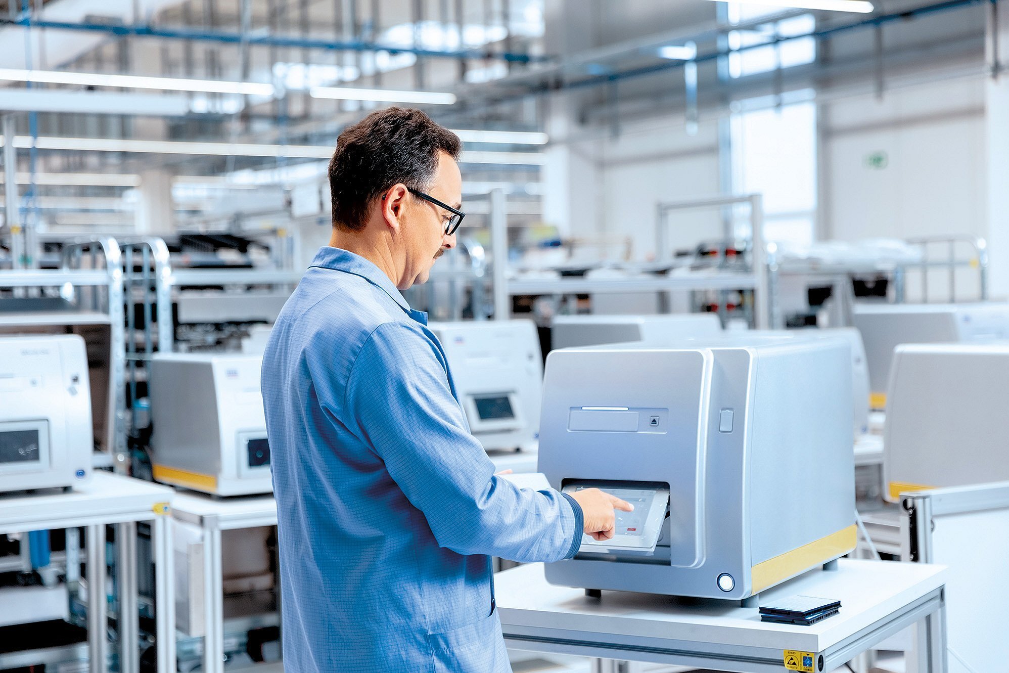 Mitarbeiter in ESD-Schutzkleidung bedient ein Prüfgerät in einer modernen Elektronikfertigung der Zollner Elektronik AG zur Qualitätssicherung
