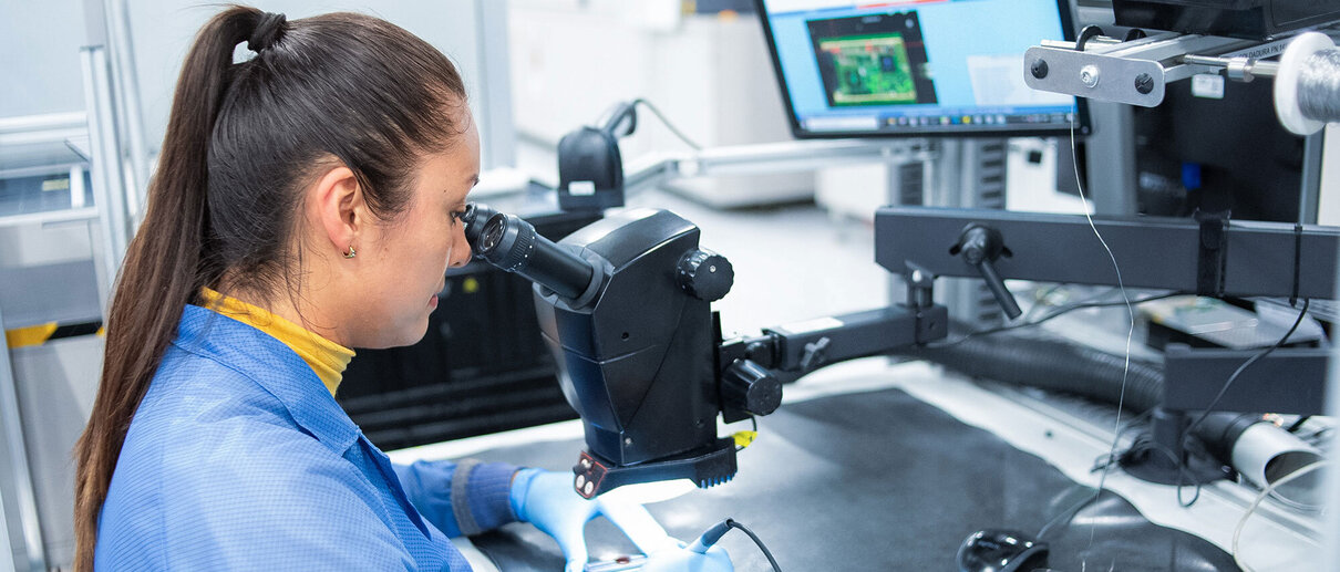 Mitarbeiterin der Zollner Elektronik AG arbeitet mit Mikroskop an elektronischer Baugruppe