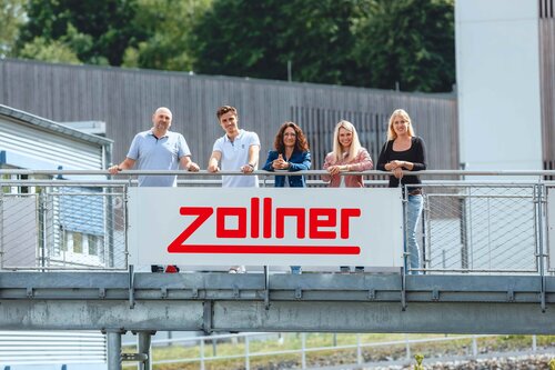 Mitarbeiter hinter einem Zollner-Firmenschild 