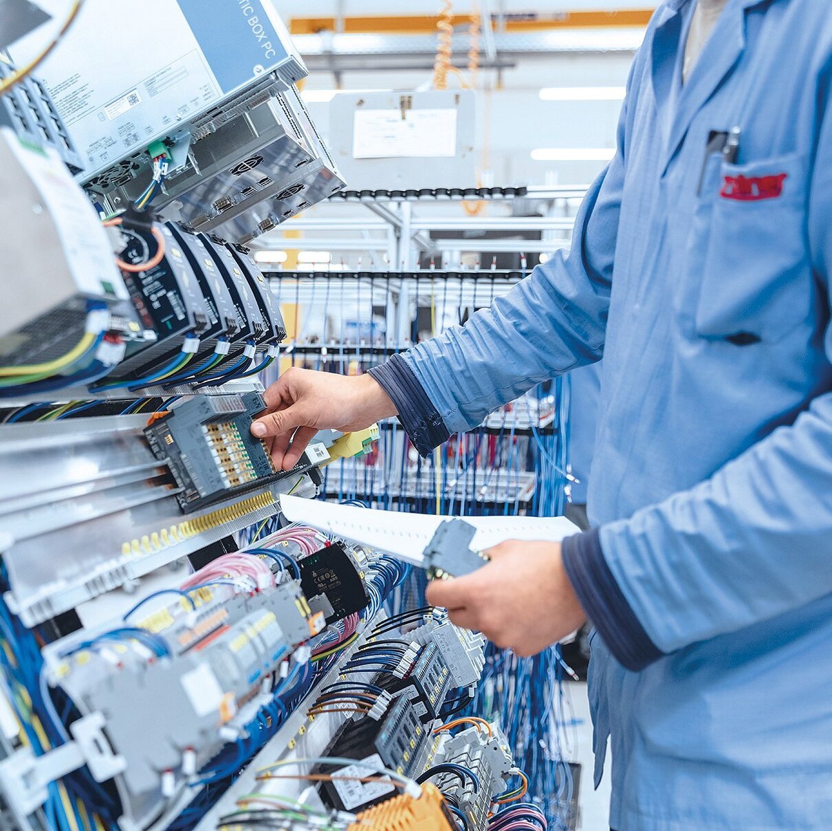 Mitarbeiter in ESD-Schutzkleidung prüft elektrische Verbindungen und Kabel an einem Schaltschrank.