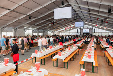 Gäste treffen ins Festzelt ein und nehmen Platz, Rot/Weiß dekoriertes Festzelt 