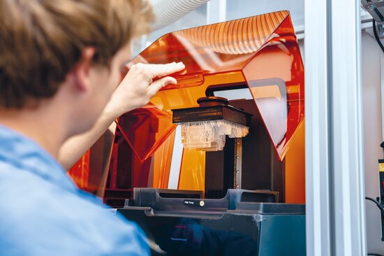 Mitarbeiter bedient 3D-Drucker für additive Fertigung in Elektronikproduktion.