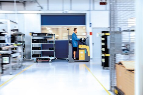 Mitarbeiter fährt auf einem elektrischen Kommissionierer durch die Produktionshalle, transportiert Materialwagen im Rahmen der Distributionslogistik.